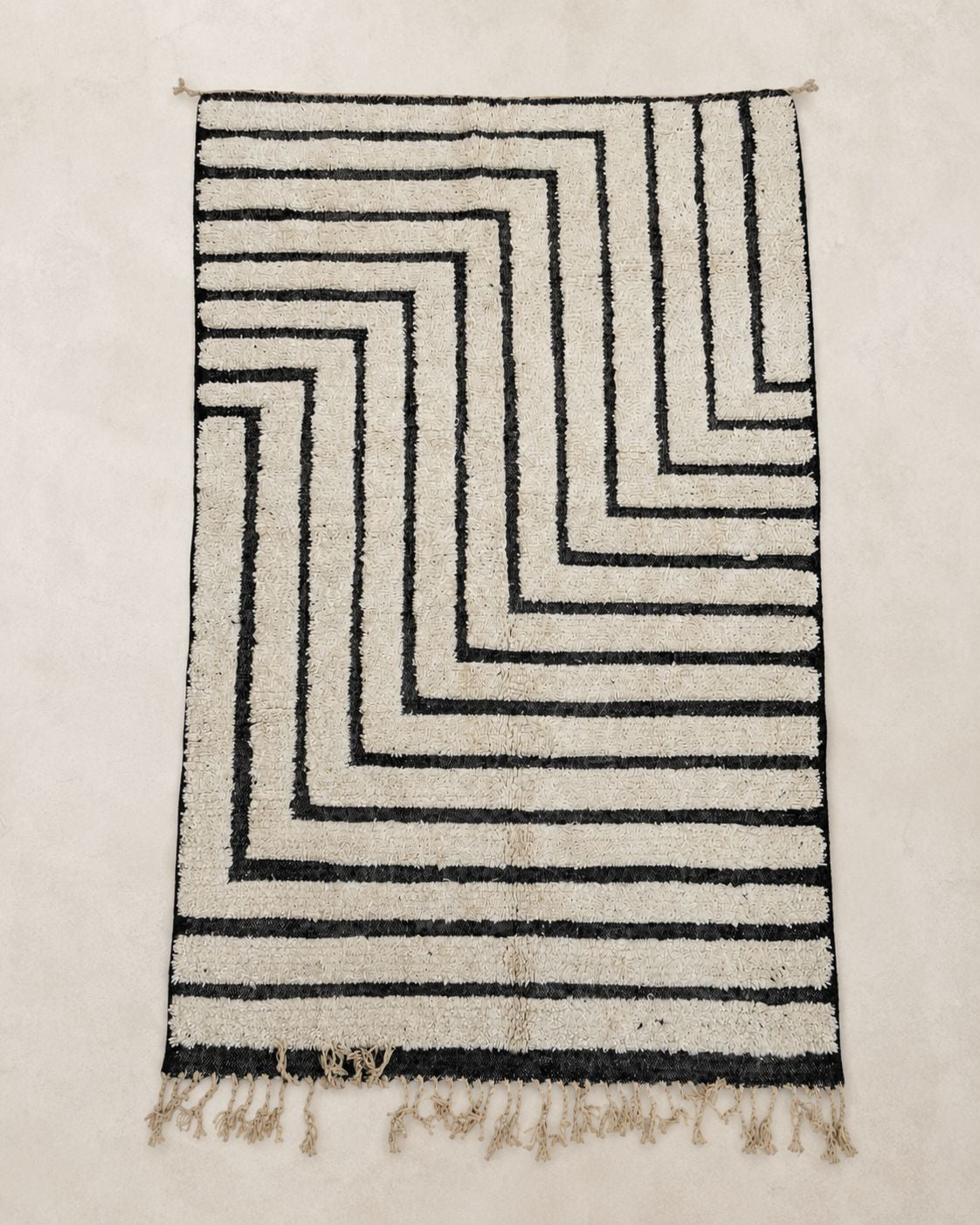 Front view of a rectangular cream rug with nested angular black lines. 