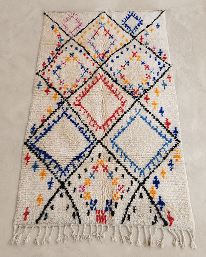 Front view of a cream Moroccan rug with black, blue, and red diamond motifs. 
