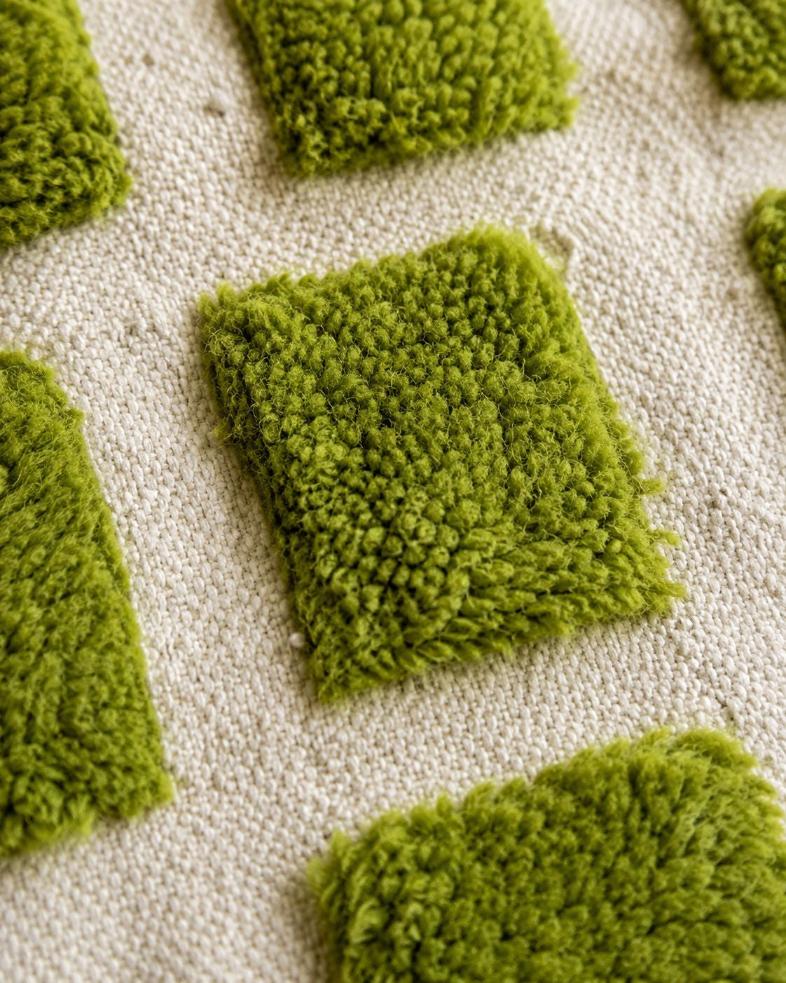 Detail view of the 100% wool high-low pile structure, showcasing the raised olive green wool blocks on a cream base.