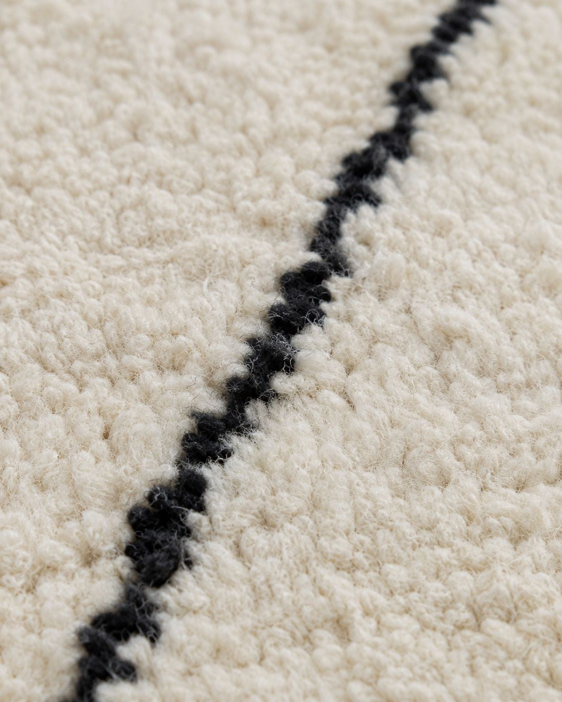 Close-up of the textured ivory wool pile and handmade black line pattern. 