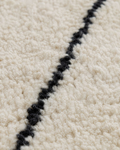 Close-up of the textured ivory wool pile and handmade black line pattern. 