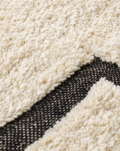 Close-up of the textured ivory wool surface and black geometric detailing. 