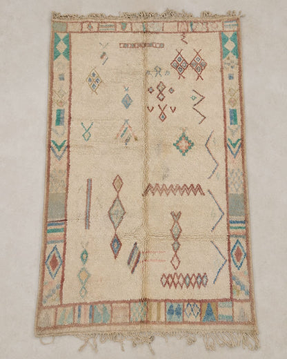 Front view of an ivory Moroccan rug with teal, blue and dusty rose symbols. 